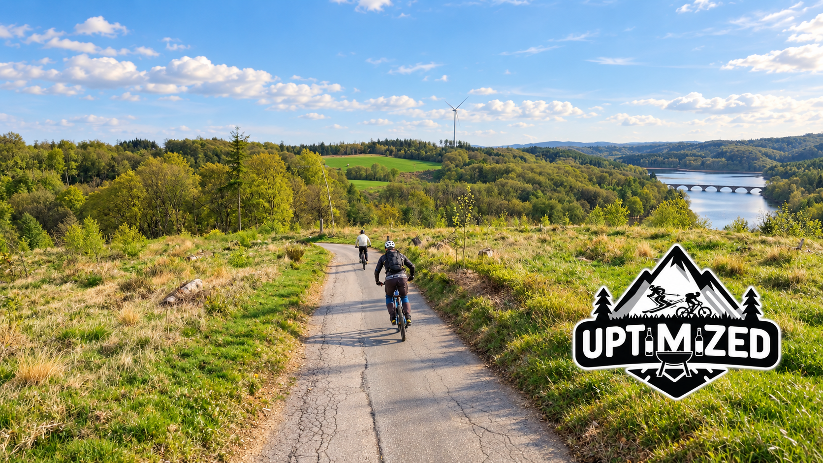 Zwei Fahrer auf einer sonnigen Tour an der Talsperre, mit sichtbarer Brücke und Uptimized-Logo unten rechts